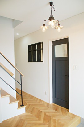 ヘリンボーンの床と黒いドアが迎える玄関